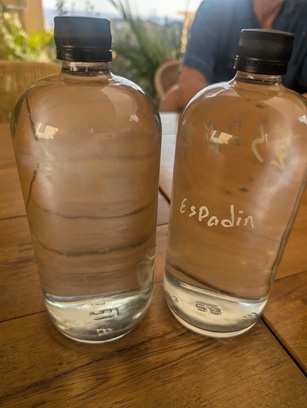 Two single liter bottles of clear Mezcal. One is labeled Espadin, the other unlabeled is Madre Cuishe